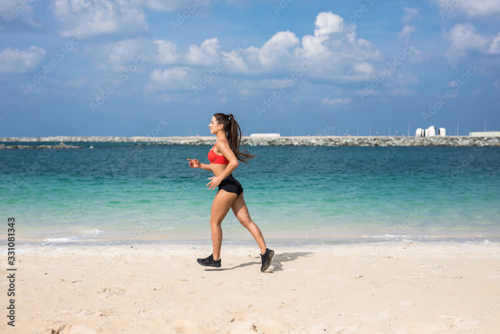 Athletic fitness woman running on the beach. Female runner jogging. Outdoor Workout.
