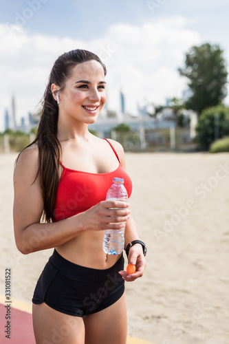 Portrait of beautiful fit woman drinking water at the sunny beach