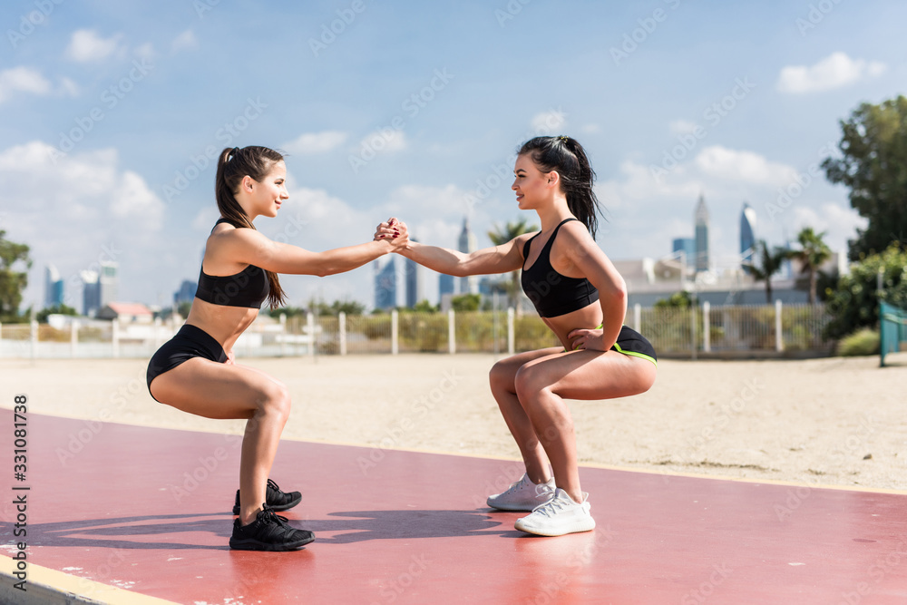 Strength in teamwork. Two young attractive women athletes exercise on the beach doing squats with a sunrise and ocean in the background. Strength in teamwork. Two young attractive women athletes exercise on the beach doing squats with a sunrise and ocean in the background.