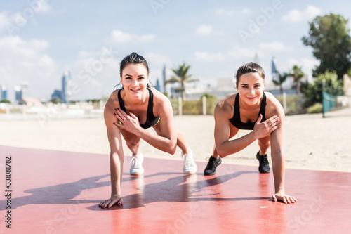 Two fitness sports girls doing sport exercises on the beach