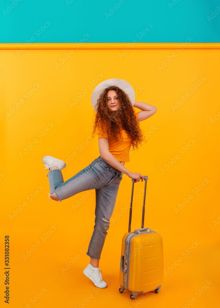 happy girl with a passport, plane tickets and a suitcase on an isolated yellow background.