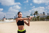 Young attractive fitness woman stretching hands on the beach