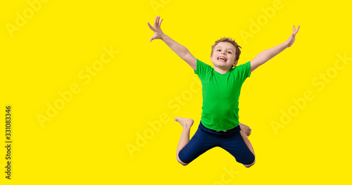 Happy little kid boy in green t-shirt on yellow background is smiling, laughing and jumping.