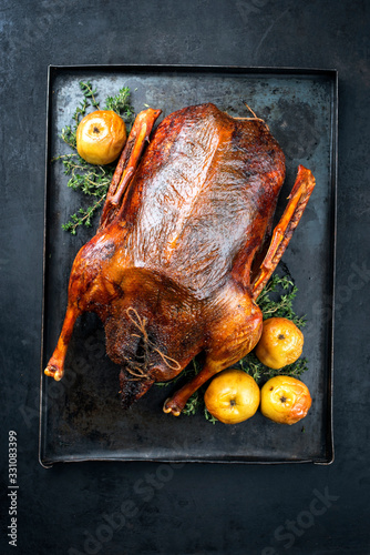 Traditional roasted stuffed Christmas goose with apples and herbs as top view on a rustic metal tray on a board