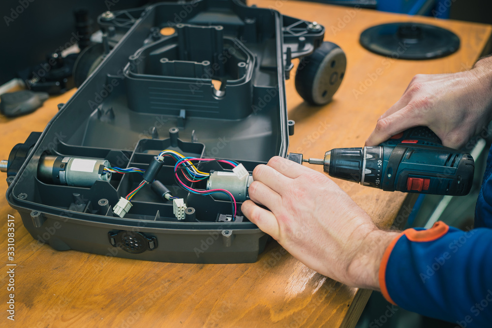 Serviceman stripping and removing electric motors on robotic lawnmower, motorized lawnmower being serviced on a table after a year of use in the mud and grass. Regular maintenance of robotic lawnmower
