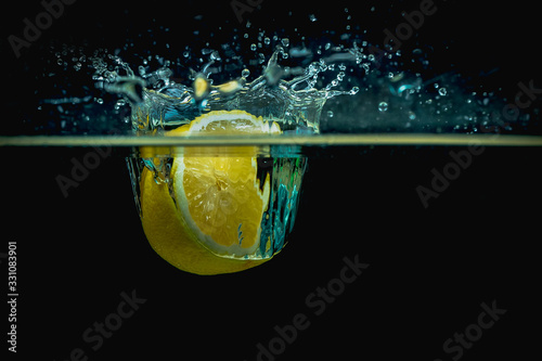 Fresh lemon half falls into water making big splash of drops and spray on a dark background. Juicy and fresh concept of lemon in water making a beautiful water crown.