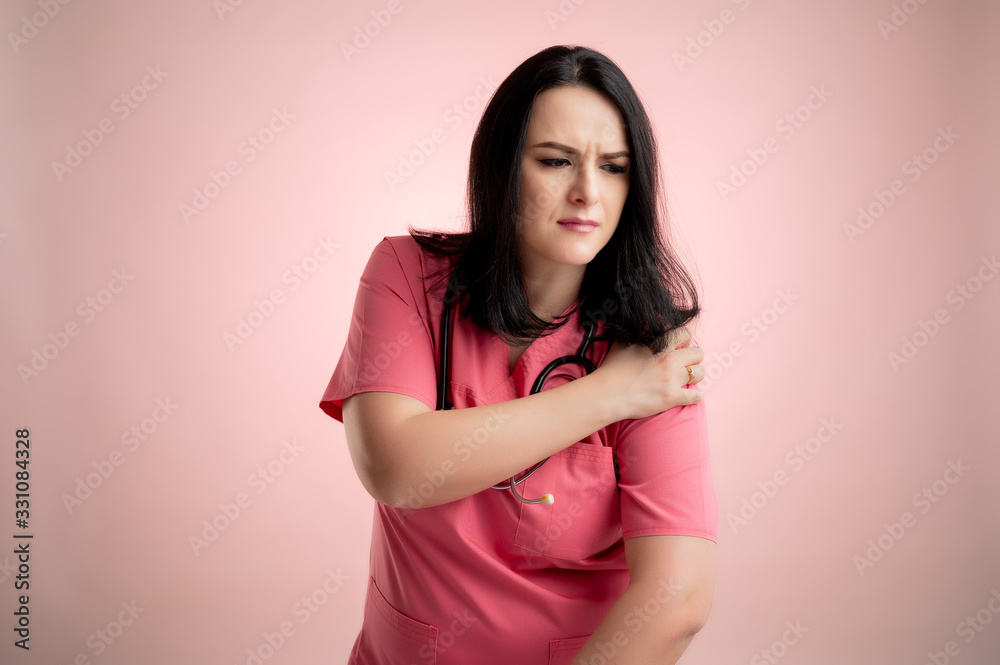 Obraz premium Beautiful woman doctor with stethoscope, wearing pink scrubs has shoulder pain