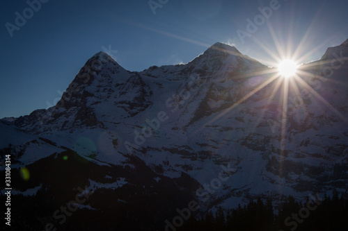 The valley of Lauterbrunnen viewed from the village of Murren in Switzerland on a sunny winter day. Panorama of swiss valley in the shadow with a strong sun flare visible © Anze
