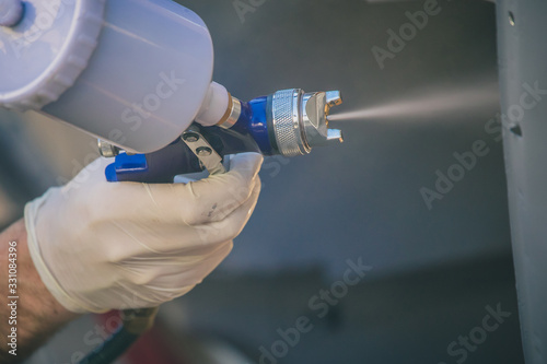 Detail of a spray gun in action. Applying lacquer or paint onto sheet metal surface using a compressed air paint gun. photo