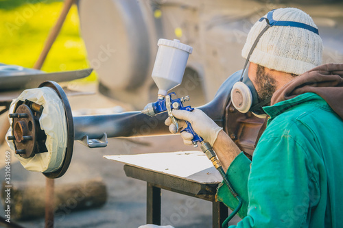 Man with automotive air spray gun in action during the restoration of a vintage car. Applying first base layer of paint onto an old big differential unit or rear axle.