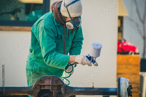 Man with automotive air spray gun in action during the restoration of a vintage car. Applying first base layer of paint onto an old big differential unit or rear axle.