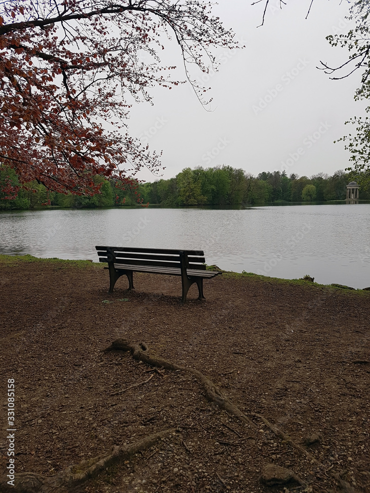 Bench near the lake on a cloudy day in spring. Empty wooden bench near the pond.