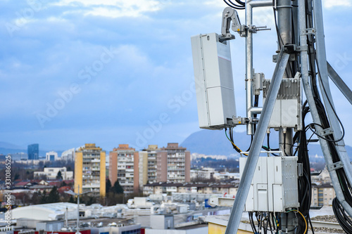 5G new radio telecommunication network antenna mounted on a metal pole providing strong signal waves from the top of the roof across big city 