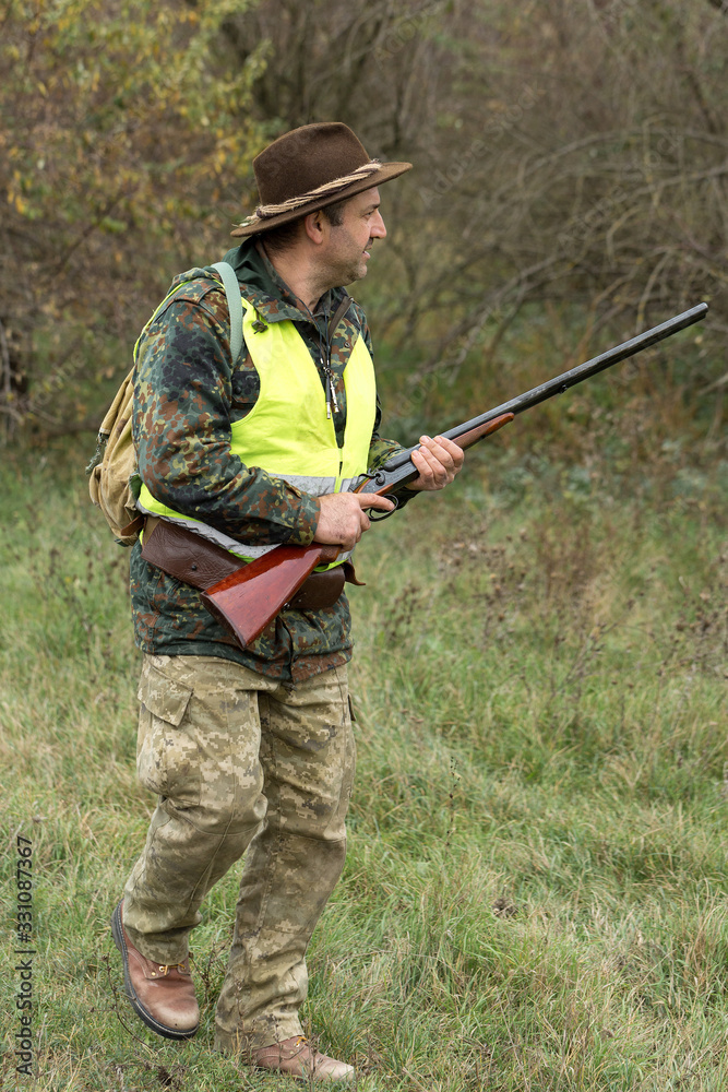 Hunting period, autumn season open. A hunter with a gun in his hands in hunting clothes in the autumn forest in search of a trophy. A man stands with weapons and hunting dogs tracking down the game.