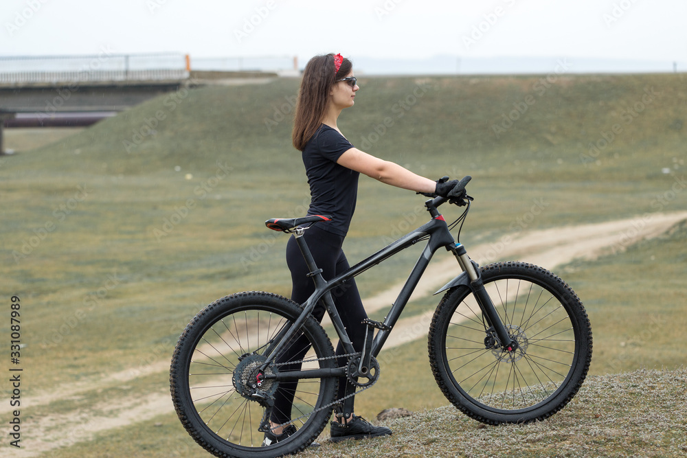 Girl on a mountain bike on offroad, beautiful portrait of a cyclist in rainy weather, Fitness girl rides a modern carbon fiber mountain bike in sportswear. Close-up portrait of a girl in red bandana. Girl on a mountain bike on offroad, beautiful portrait of a cyclist in rainy weather, Fitness girl rides a modern carbon fiber mountain bike in sportswear. Close-up portrait of a girl in red bandana.