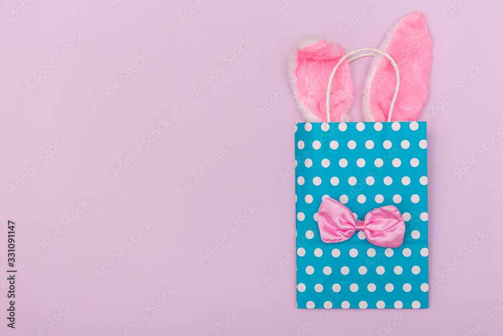 Minimalistic pastel image with blue gift bag with Easter bunny ears and the bow tie on pink background with copy space. Minimalistic pastel image with blue gift bag with Easter bunny ears and the bow tie on pink background with copy space.