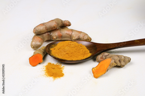Turmeric powder in a wooden spoon and fresh turmeric roots isolated on a white background is an ingredient in turmeric foods and ingredients in skin care products. Turmeric helps the skin to be strong