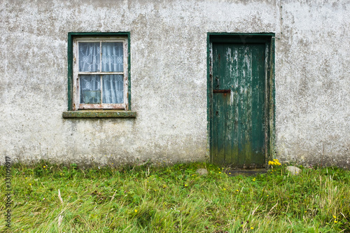 Run down Irish cottage with green door and window with chipped paint 