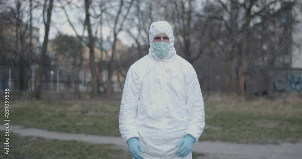 Portrait of male scientist in protective suit showing thumbs up standing in urban daytime park after pandemic coronavirus quarantine time has ended looking in camera 4K Portrait of male scientist in protective suit showing thumbs up standing in urban daytime park after pandemic coronavirus quarantine time has ended looking in camera 4K