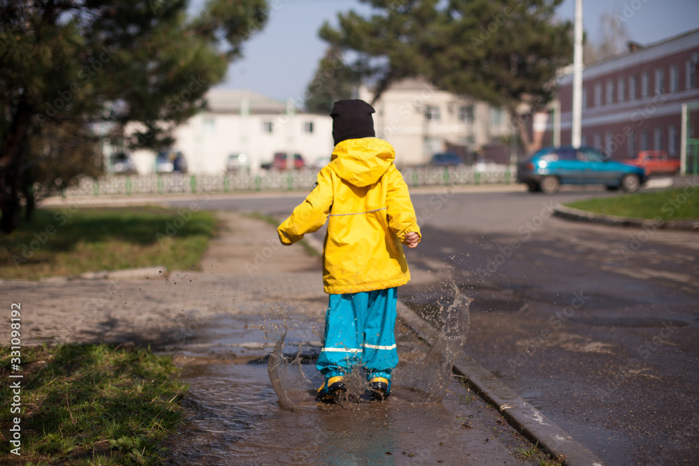 Happy child jumping in a puddle in a waterproof spray suit in all directions useful walks around the city. Happy child jumping in a puddle in a waterproof spray suit in all directions useful walks around the city.