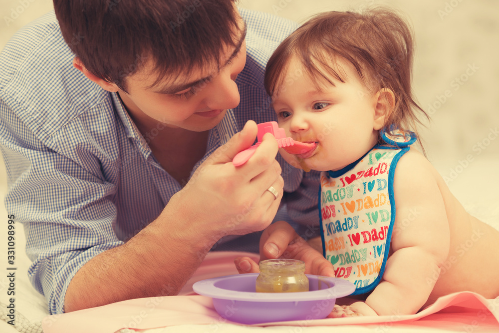 Happy young father feeding baby girl on blanket at home Happy young father feeding baby girl on blanket at home