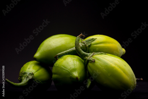 Lot of lot of vibrant green scarlet eggplant vegetable on top of each other against a black background. Graphic minimalist image of food. photo