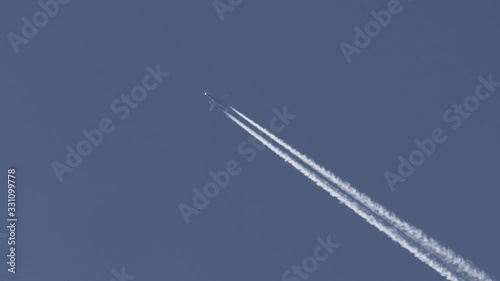 Airplane flying over a clear blue sky and leaving white contrails behind.