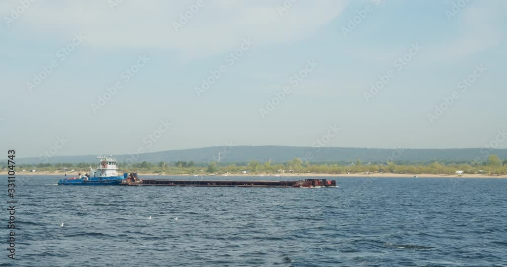 Long shot, empty cargo barge floating on the river. Transportation of goods by water using tugboats. Long shot, empty cargo barge floating on the river. Transportation of goods by water using tugboats.