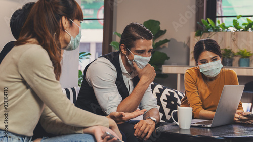 caucasian and asian working together in business lobby of coworking space and everyone wearing medical mask to protect from coronavirus covid 19 infection, working in coronavirus outbreak situation
