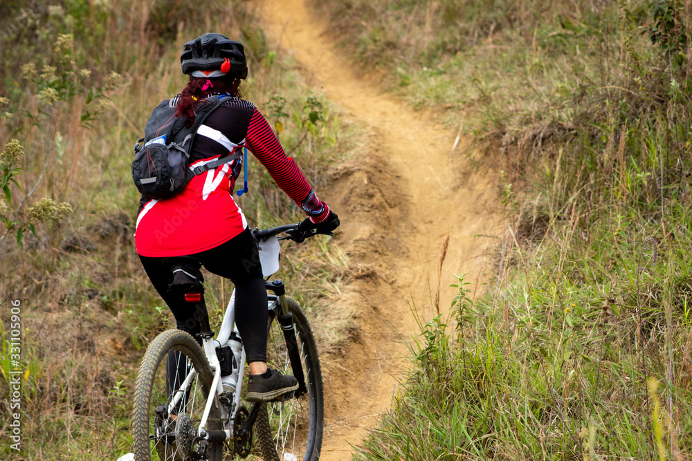 female cyclist from back with red uniform in mountain biking competition going up female cyclist from back with red uniform in mountain biking competition going up