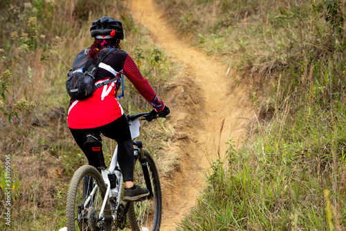  female cyclist from back with red uniform in mountain biking competition going up
