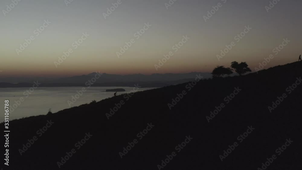 Silhouette of a man hiking on a hill top with late Sunset light over Padar island and bay, Indonesia, Aerial follow footage. Silhouette of a man hiking on a hill top with late Sunset light over Padar island and bay, Indonesia, Aerial follow footage.