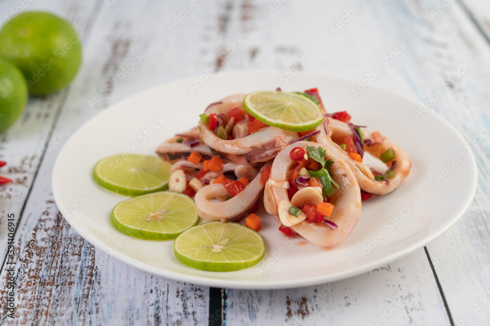 Spicy lemon squid with galangal, chilies, carrots, peppermint, spring onions and garlic on a plate on a white wooden floor. Spicy lemon squid with galangal, chilies, carrots, peppermint, spring onions and garlic on a plate on a white wooden floor.