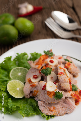 Spicy lime pork with salad, galangal, chilli, tomato and garlic on a white plate on a wooden floor.