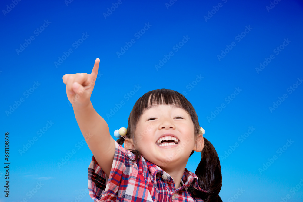 青空を背景に元気よく指差しをする幼い女の子。元気,前向き、快活イメージ