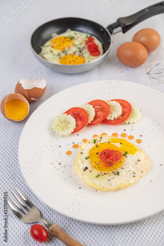 Fried egg on a white plate with sliced ​​Spring onion and sliced ​​tomatoes