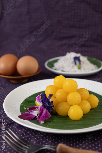 Thong Yod dessert on a banana leaf in a white plate with orchids and a fork