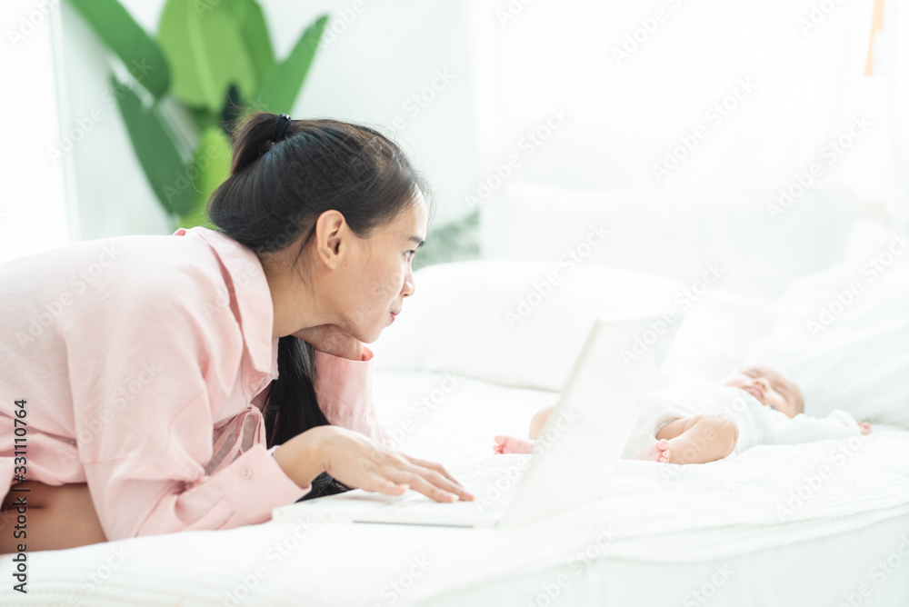 Young happy mother asian woman work on laptop on bed take care newborn sleep, work at home and nursery care concept. Young happy mother asian woman work on laptop on bed take care newborn sleep, work at home and nursery care concept.