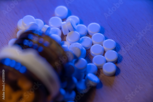 Pain killers in a bottle, opioids and medicinals. Medical opioid epidemic. White pills under blue light and a brown glass bottle
