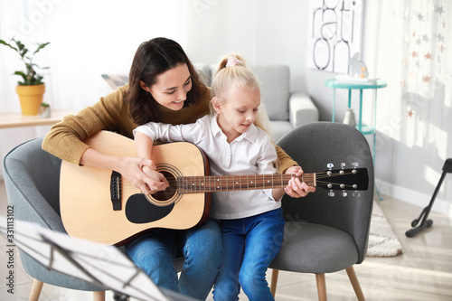 Private music teacher giving guitar lessons to little girl at home