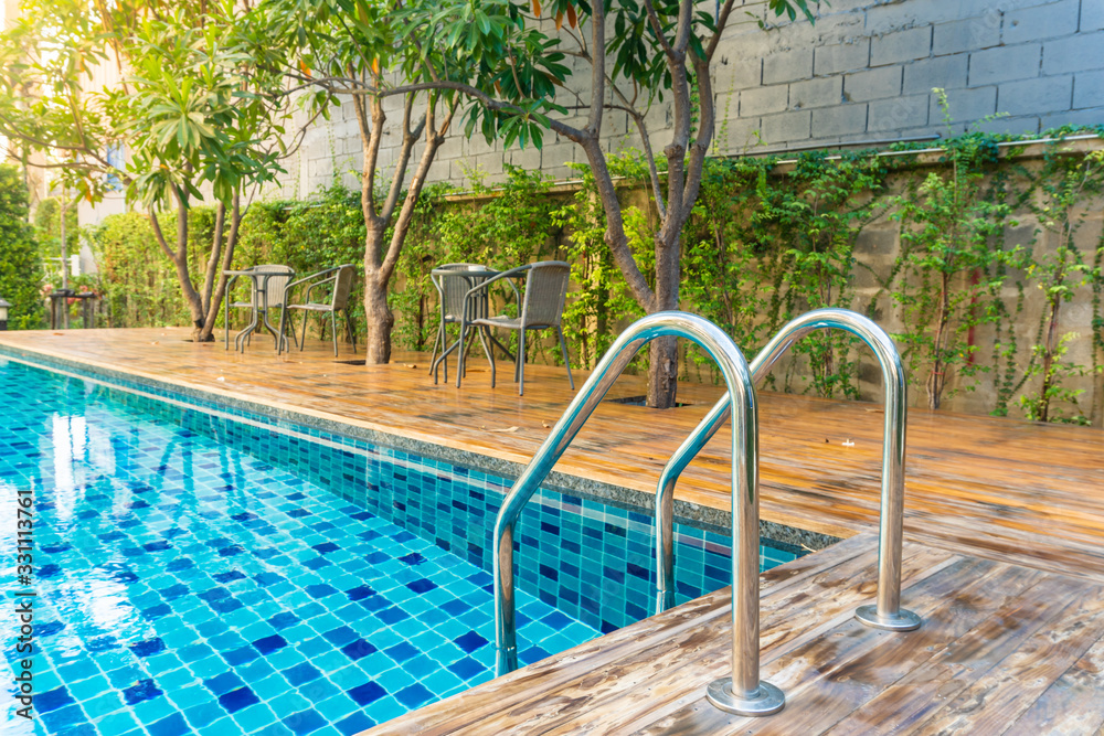 Swimming pool with stair at hotel with decorated with trees and chairs for relaxing