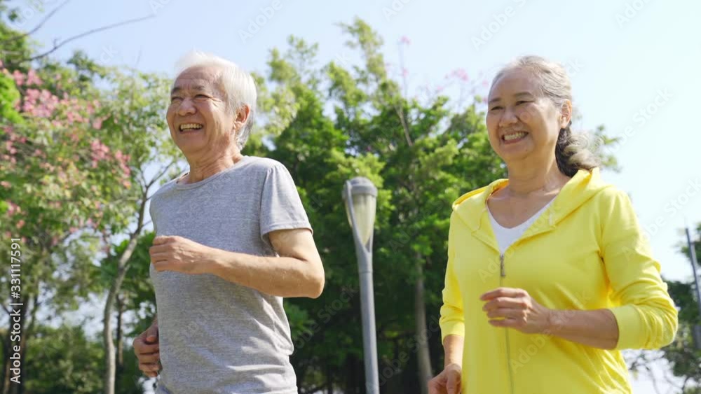 happy senior asian couple jogging running exercising outdoors in a park