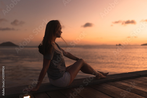 Beautiful girl at sunset on the sea in Thailand. Bright orange and yellow pink sky. Girl traveler enjoys the view. Woman in the tropics