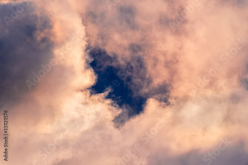 Close up of storm clouds colored in sunset colors; break in the clouds reveals dark blue sky