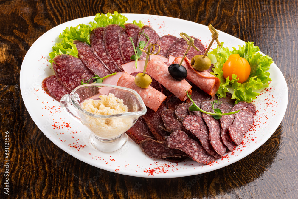sausage sliced on a white dish with olives and salad on a wooden background sausage sliced on a white dish with olives and salad on a wooden background