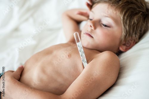 sick small caucasian lying in bed boy with thermometr in hospital photo