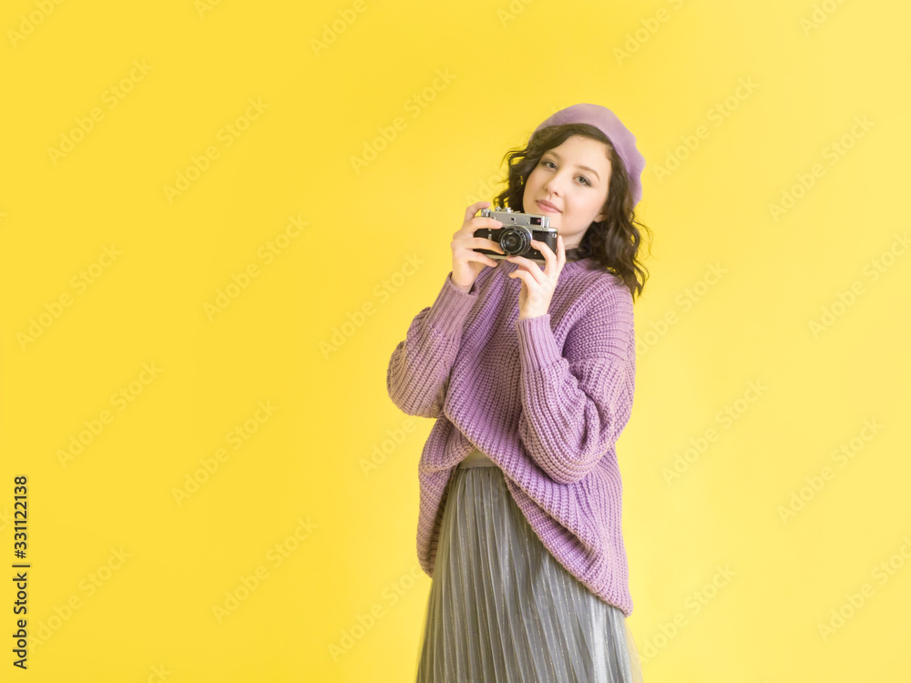 Obraz premium Fashionable girl in a lilac sweater and beret with a retro camera in her hands. Yellow background