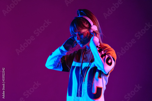 Calm girl wear stylish glasses, headphones listen music at purple background.