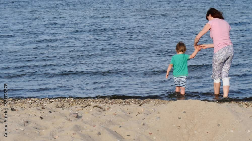 Mother playing with little child boy on sand beach. Adult woman and her son enjoying summer day on seshore. Family holiday at sea. Slow motion Mother playing with little child boy on sand beach. Adult woman and her son enjoying summer day on seshore. Family holiday at sea. Slow motion
