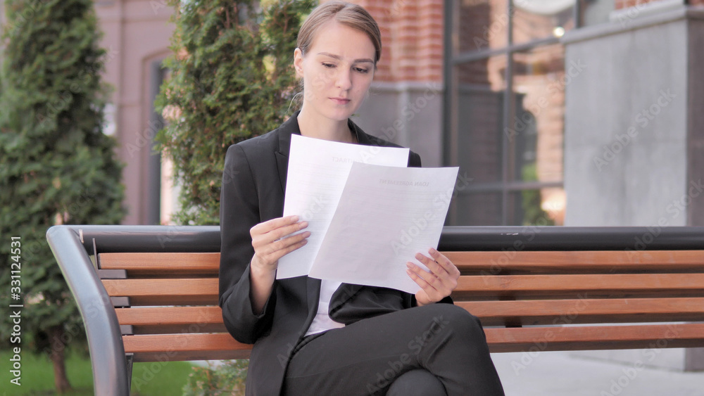 Young Businesswoman Reading Documents while Sitting Outdoor on Bench Young Businesswoman Reading Documents while Sitting Outdoor on Bench